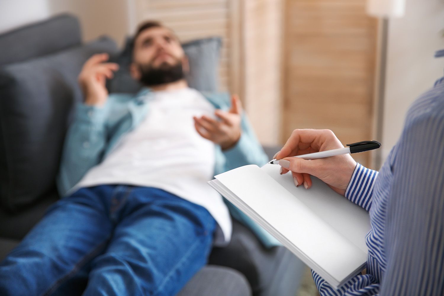 Therapist taking notes while person lies on couch talking