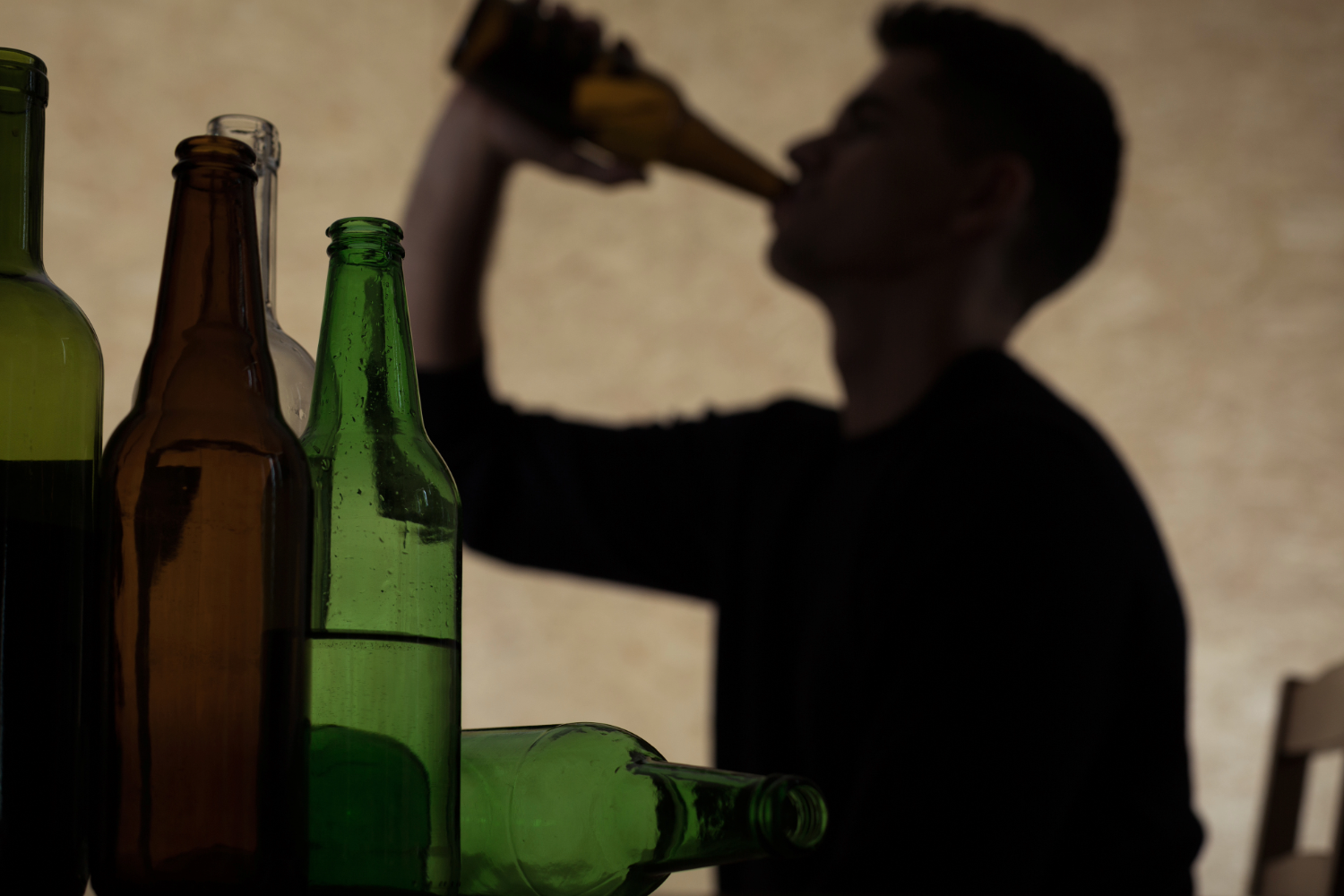 Silhouette of person drinking from a bottle with empty bottles