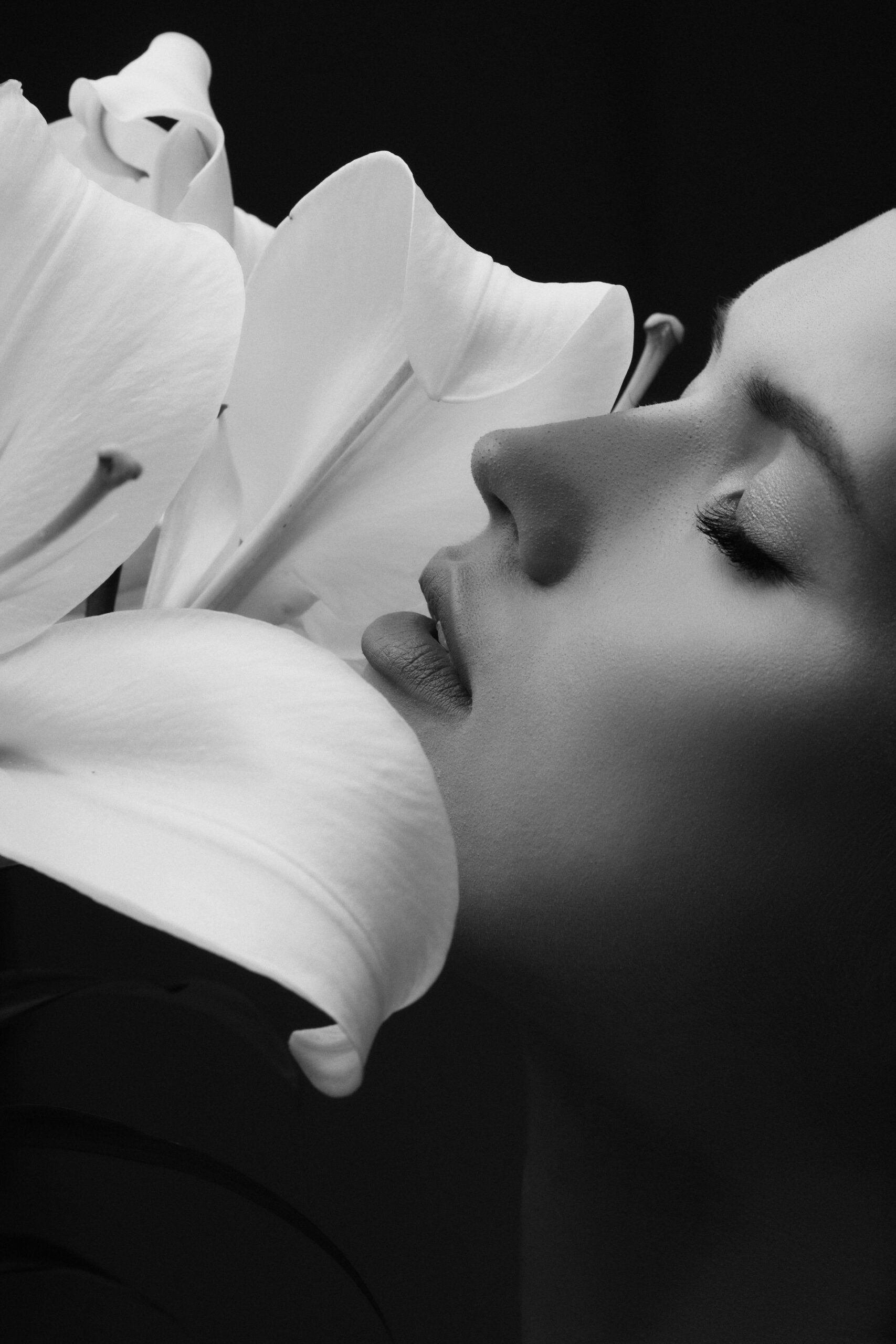 Woman's face close to large white lily eyes closed